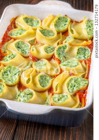 Golden baked lumaconi filled with ricotta and spinach resting in rich tomato sauce 132714179