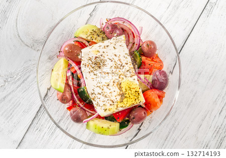 Fresh traditional Greek salad topped with thick feta slice served in glass bowl 132714193