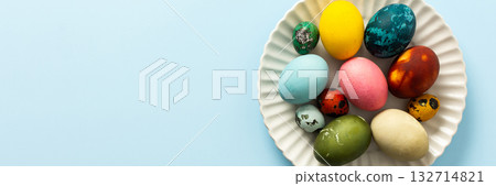 A variety of decorated Easter eggs in vibrant colors are creatively arranged on a white plate set against a soft blue background, symbolizing spring festivities and joy, banner A variety of decorated Easter eggs in vibrant colors are creatively arranged on a white plate set against a soft blue background, symbolizing spring festivities and joy, banner 132714821