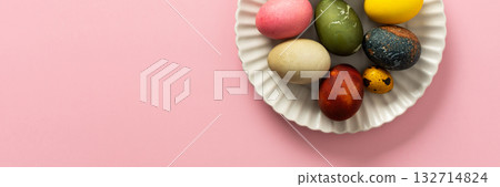 A variety of decorated Easter eggs are arranged on a circular plate against a soft pink background, showcasing vibrant colors and intricate designs for a seasonal celebration, banner A variety of decorated Easter eggs are arranged on a circular plate against a soft pink background, showcasing vibrant colors and intricate designs for a seasonal celebration, banner 132714824