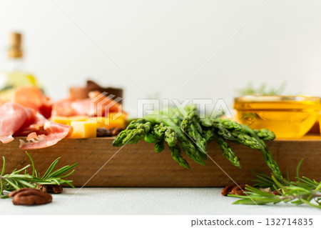 A vibrant charcuterie board is set for a gathering, showcasing fresh asparagus, assorted cheeses, cured meats, and nuts. This setup invites guests to enjoy tasty bites together 132714835