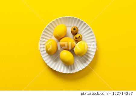 Bright yellow Easter eggs and speckled quail eggs are beautifully arranged on a white plate, creating a cheerful centerpiece perfect for spring festivities and family gatherings 132714857