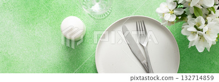 A lovely spring table setting features a white plate, silverware, and elegant glassware, complemented by fresh flowers and a soft green background, perfect for gatherings and meals, banner 132714859