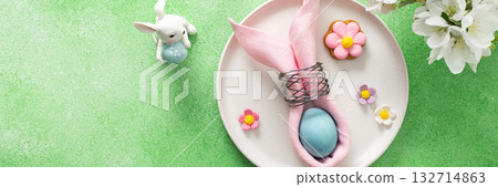 A beautifully arranged table setting for Easter features a pink napkin wrapped around an egg, surrounded by floral decorations and colorful candies, banner 132714863