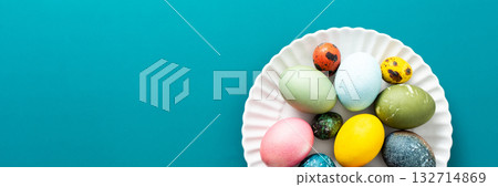 A beautiful assortment of Easter eggs in various colors and patterns is displayed on a round white plate against a bright blue background, perfect for holiday festivities, banner A beautiful assortment of Easter eggs in various colors and patterns is displayed on a round white plate against a bright blue background, perfect for holiday festivities, banner 132714869