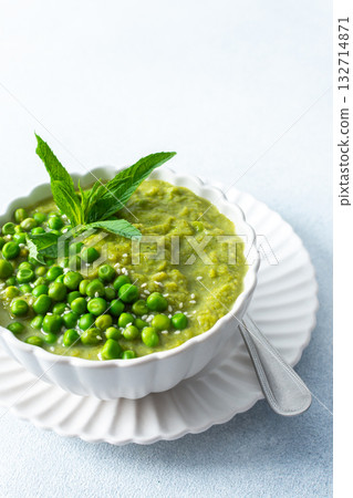A bowl of vibrant green pea and broccoli soup is topped with fresh mint leaves for flavor. This healthy dish is perfect for a warm lunch or cozy dinner at home 132714871