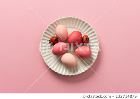 A collection of pink and white Easter eggs placed on a white plate, set against a soft pink background, showcasing festive decorations for spring festivities 132714879