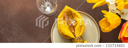 A beautifully arranged spring table setting features a light plate, gold-tone utensils, and vibrant flowers. The yellow napkin adds a pop of color, creating a joyful atmosphere for dining, banner 132714881