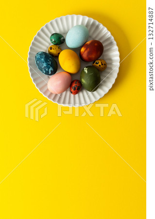 A white plate holds an assortment of vibrant Easter eggs in various colors, placed on a sunny yellow backdrop, perfect for a festive spring gathering A white plate holds an assortment of vibrant Easter eggs in various colors, placed on a sunny yellow backdrop, perfect for a festive spring gathering 132714887