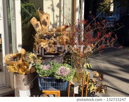Autumn flower shop display with dry bouquets and red berries. Seasonal street decor, natural composition and urban charm. Autumn flower shop display with dry bouquets and red berries. Seasonal street decor, natural composition and urban charm. 132715247