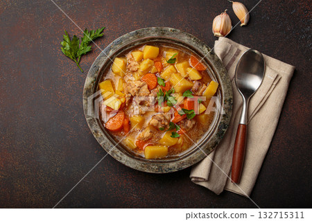 Chicken stew or soup with potatoes and carrots served in rustic bowl with spoon top view on dark brown concrete background 132715311