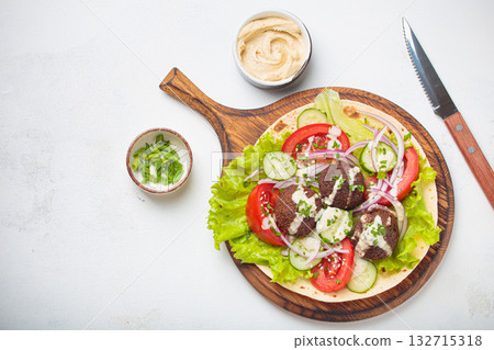 Preparing and cooking falafel wrap on pita on wooden cutting board with hummus top view white background, space for text Preparing and cooking falafel wrap on pita on wooden cutting board with hummus top view white background, space for text 132715318