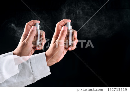 A hand in a white shirt sprays perfume or air freshener. Black background. 132715519