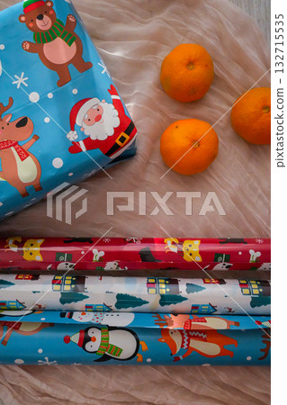 A vertical composition of a wrapped Christmas gift box and three rolls of colorful wrapping paper. Perfect for festive holiday, seasonal, and DIY projects. 132715535