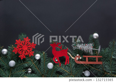 Christmas festive fairy frame and greeting card. A toy of red deer drive by sledge a Christmas tree on black background with copy space. Top view. Christmas festive fairy frame and greeting card. A toy of red deer drive by sledge a Christmas tree on black background with copy space. Top view. 132715565
