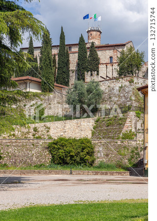 View of Brescia Castle on Cidneo Hill showing stone walls terraces towers and cypress trees in light 132715744