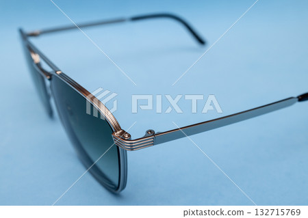Fashion inspired seventies style photo of sleek silver sunglasses on pastel blue smooth backdrop 132715769