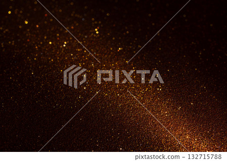 Illuminated brown glitter texture glowing from lower right with golden fragments across deep shadow 132715788