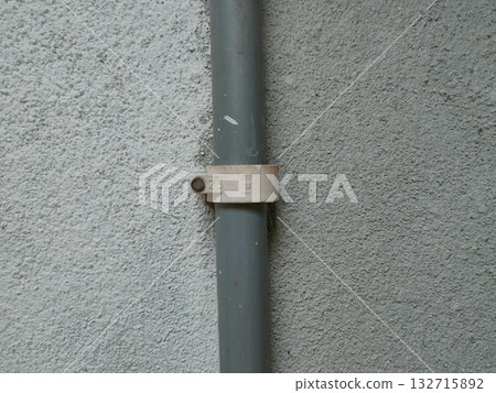The image shows a PVC pipe with a pipe clip or saddle clamp. This type of clamp is used to secure the pipe to a wall or other surface. 132715892