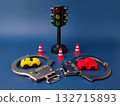 The image shows a miniature traffic light, a toy car, a pair of handcuffs, and several traffic cones on a blue background. 132715893