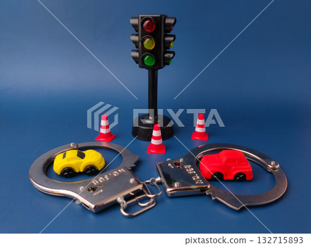 The image shows a miniature traffic light, a toy car, a pair of handcuffs, and several traffic cones on a blue background. The image shows a miniature traffic light, a toy car, a pair of handcuffs, and several traffic cones on a blue background. 132715893