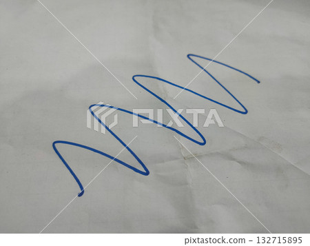 The image shows a blue, continuous, wavy line drawn on a piece of white paper. The image shows a blue, continuous, wavy line drawn on a piece of white paper. 132715895