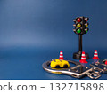 The image shows a miniature traffic light, a toy car, a pair of handcuffs, and several traffic cones on a blue background. 132715898