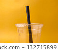 The image shows a clear disposable plastic cup with a lid and a black straw on a yellow background. 132715899