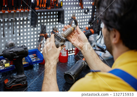 Service man repairing a broken power drill inside a busy workshop Service man repairing a broken power drill inside a busy workshop 132715933