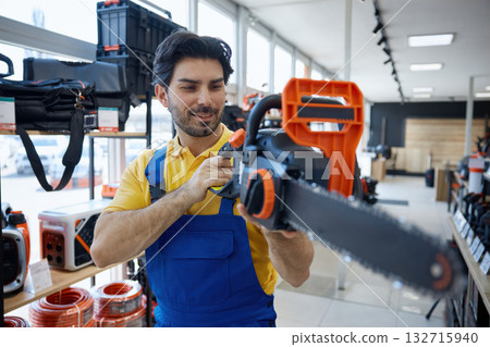 Worker is standing in a store holding a chainsaw tool Worker is standing in a store holding a chainsaw tool 132715940