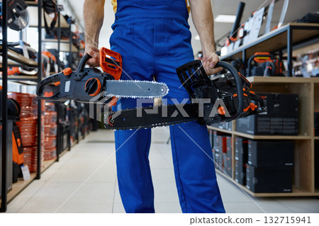 A man worker holding two chainsaws inside a store A man worker holding two chainsaws inside a store 132715941