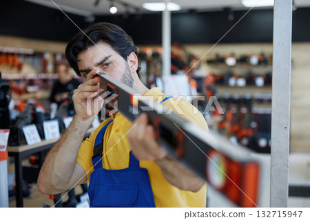A man worker taking measurements using a bubble level tool inside a store A man worker taking measurements using a bubble level tool inside a store 132715947