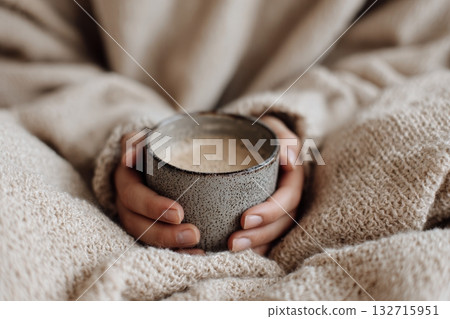 Faceless hands holding coffee mug on beige blanket with cozy minimalist vibe and soft light 132715951