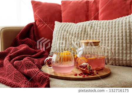 Glass Teapot and Teacup with Pomegranate Drink with Ginger and Citrus on Cozy Sofa with Autumn Decor Glass Teapot and Teacup with Pomegranate Drink with Ginger and Citrus on Cozy Sofa with Autumn Decor 132716175