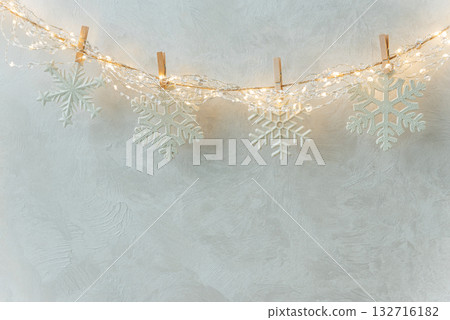 White Snowflake Ornaments Hanging on String Lights Against Textured Wall White Snowflake Ornaments Hanging on String Lights Against Textured Wall 132716182
