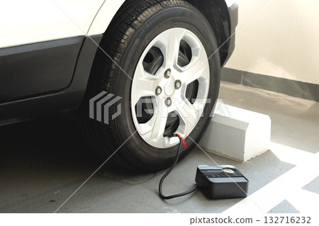 Car tire being inflated with portable electric air compressor in parking garage. Vehicle maintenance concept. 132716232