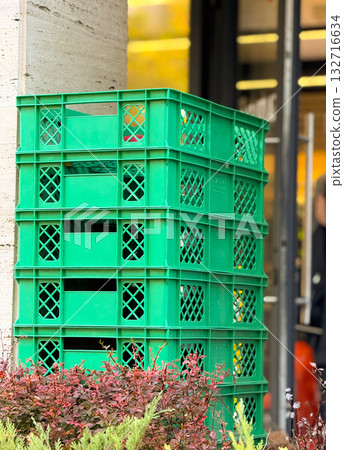 Stack of green plastic crates near store entrance. Urban storage, retail logistics and everyday street life. 132716634