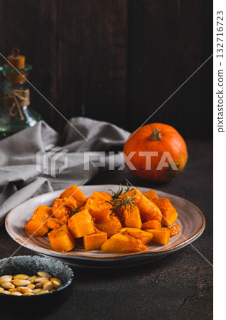 Pieces of baked pumpkin with rosemary on a plate on the table vertical view Pieces of baked pumpkin with rosemary on a plate on the table vertical view 132716723