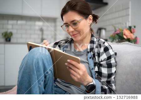 Happy Girl Sitting On The Sofa At Home Writing In A Notebook Happy Girl Sitting On The Sofa At Home Writing In A Notebook 132716988