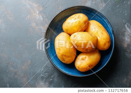 Freshly Harvested Yellow Potatoes in a Blue Bowl on a Textured Surface 132717656
