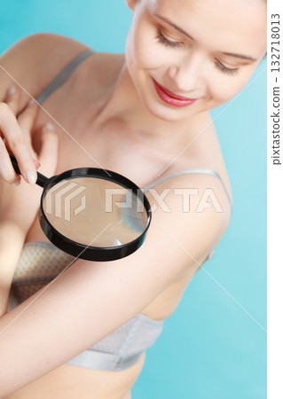 Woman using magnifying glass to examine her moles skin Woman using magnifying glass to examine her moles skin 132718013