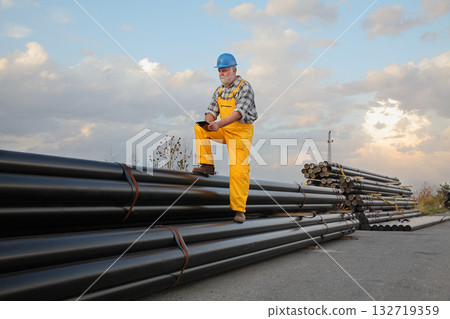 Worker at construction site with heap of pipes Worker at construction site with heap of pipes 132719359