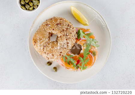 Bagel with salmon, cream cheese, cucumber and arugula on white background. Top view.  132720220