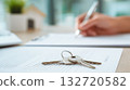 House keys on contract with person signing in blurred background near model home. Real estate closing, contract finalization, mortgage approval, moment of property transfer 132720582