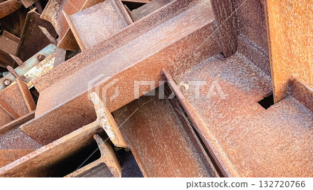 Close-up of a chaotic pile of heavily rusted metal I-beams, creating an industrial abstract background texture 132720766