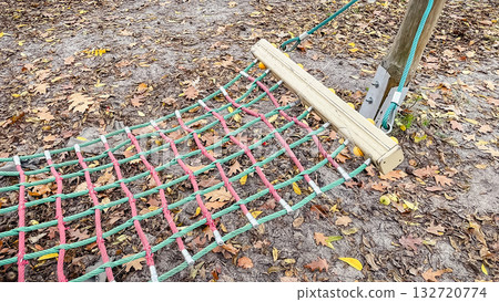 Colorful rope climbing net resting on the ground covered with brown autumn leaves and acorns Colorful rope climbing net resting on the ground covered with brown autumn leaves and acorns 132720774