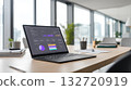 Laptop displaying a business intelligence dashboard with charts and graphs rests on light wooden conference table in bright modern office with large windows 132720919