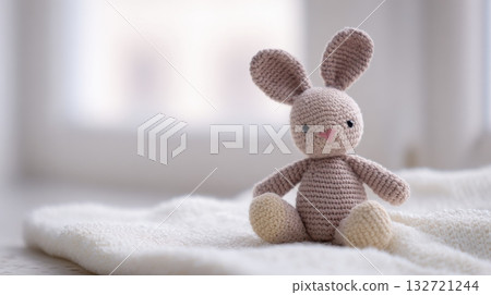 Crocheted Bunny Toy On Soft Blanket In Bright Room. Handmade Craft For Children'S Comfort And Play Crocheted Bunny Toy On Soft Blanket In Bright Room. Handmade Craft For Children'S Comfort And Play 132721244