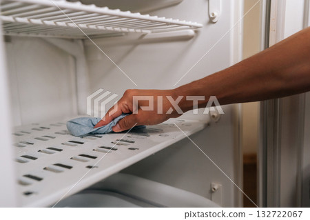 Person defrosting and cleaning interior of refrigerator using blue rag to wipe away ice and grime buildup, ensuring fresh and sanitary food storage environment. Concept of hygiene and cleanliness. 132722067
