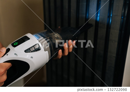 Close-up of housekeeper using portable vacuum cleaner to remove dust and debris from grill of refrigerator, ensuring cleanliness and hygiene in home kitchen. Concept of domestic work, housekeeping Close-up of housekeeper using portable vacuum cleaner to remove dust and debris from grill of refrigerator, ensuring cleanliness and hygiene in home kitchen. Concept of domestic work, housekeeping 132722098